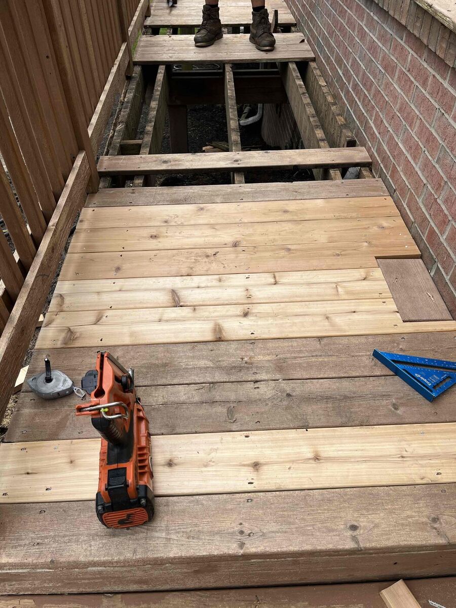 New cedar deck boards being installed next to older weathered decking during a board replacement repair, Northville MI